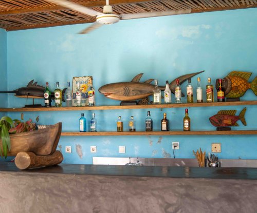Bar at Omali with blue walls, wooden fish sculptures and spirit bottles on open shelves, São Tomé Island