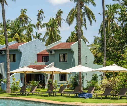 View from the pool at Omali with sun loungers, parasols and pastel-coloured buildings framed by tall palm trees, São Tomé Island