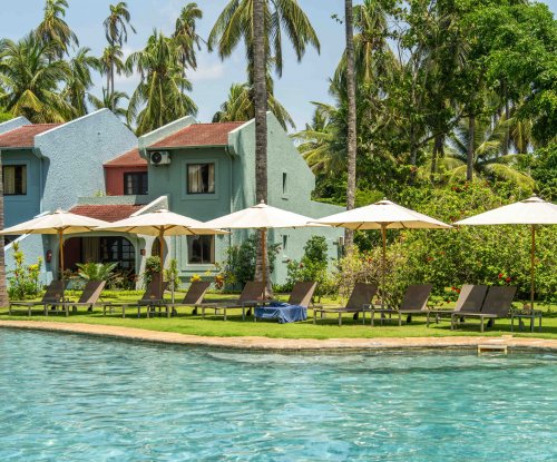 Sun loungers and parasols by the pool at Omali, with pastel-coloured buildings and palm trees in the background, São Tomé Island