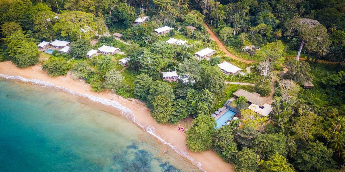 Aerial view of the sea, beach, and small huts in the green forest at Sundy Praia