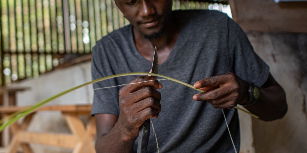 Local man in a hat and jeans weaving baskets on Príncipe Island.