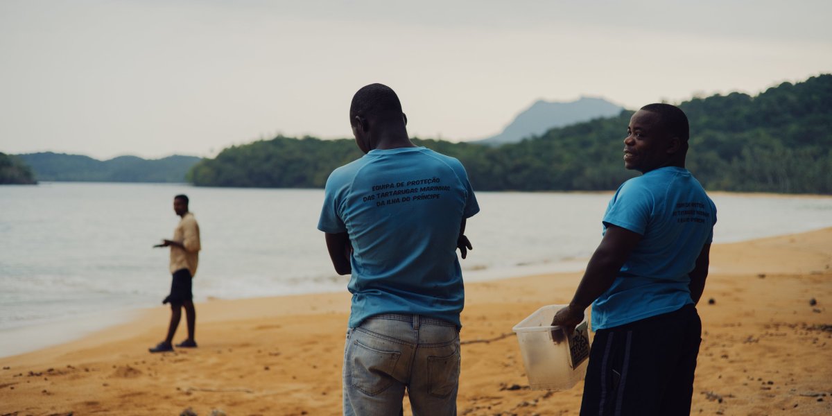 Três locais na praia de Principe Island, um com um recipiente de plástico na mão.