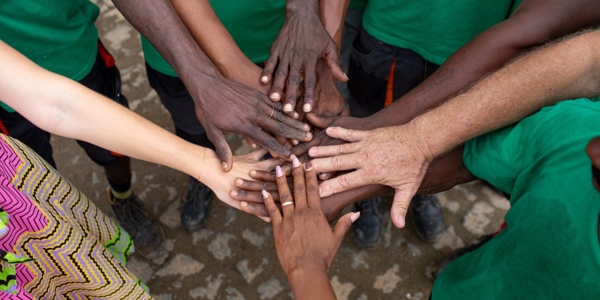 Círculo de mãos com diferentes tons de pele a tocar-se no centro na Ilha do Príncipe.