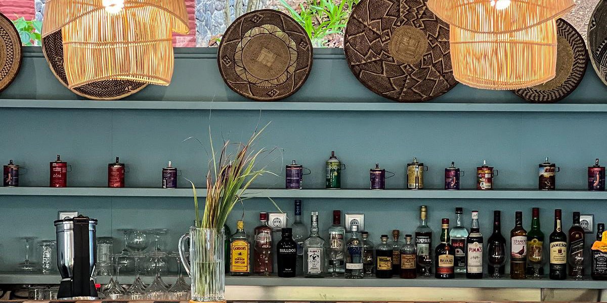 Área do bar no Bom Bom Beach Resort com luminárias de vime e prateleiras com garrafas.