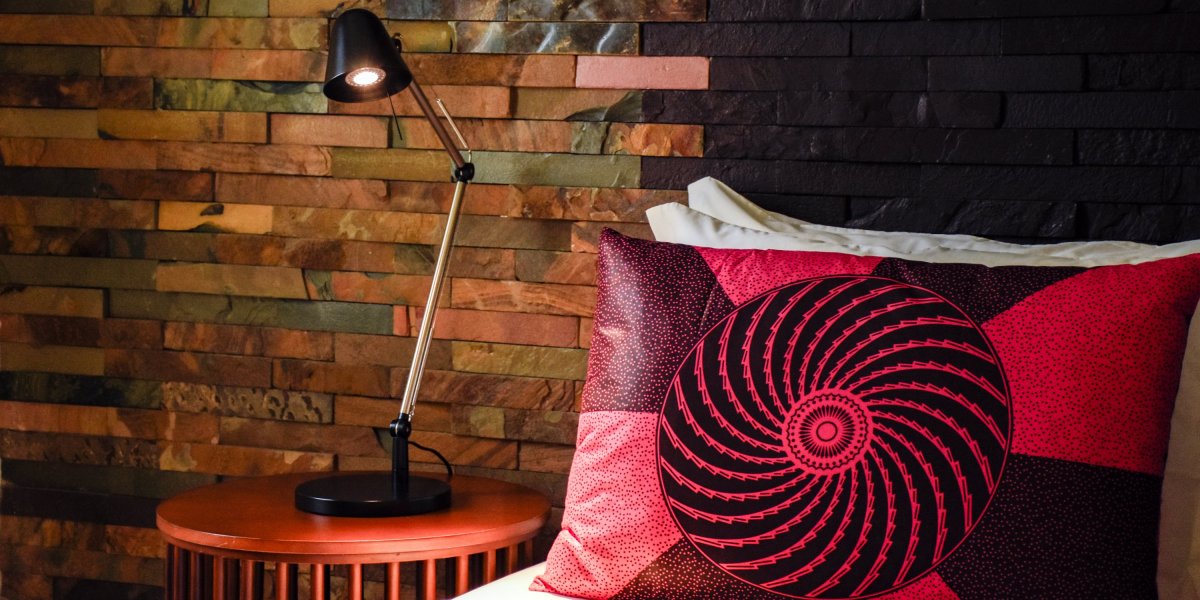 Bed with red patterned cushion and stone wall at Omali.