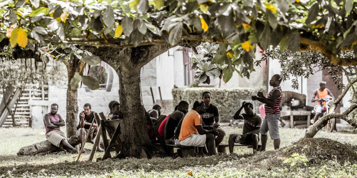 Locals sitting together under a tree in front of Roca Sundy on Príncipe Island.