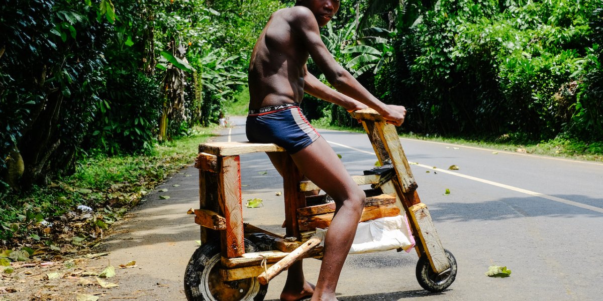 Boy on a handmade wooden bicycle on a tropical road, Príncipe Island