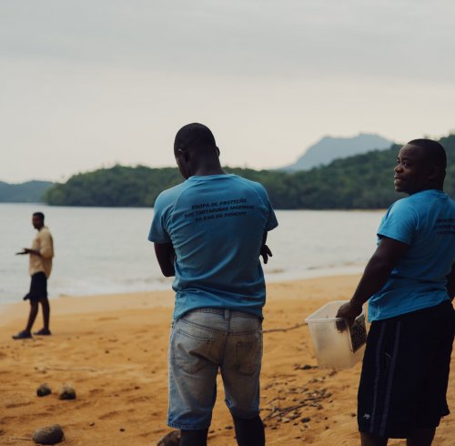 Three locals on Principe Island beach, one holding a plastic container.