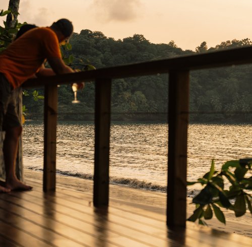 A man holding a drink at the beach during sunset at Bom Bom Beach Resort.