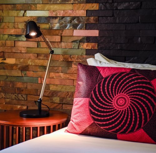 Bed with red patterned cushion and stone wall at Omali.