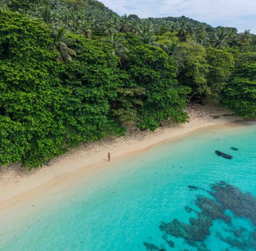 Vista aérea de praia isolada com rochas vulcânicas, areia dourada e águas turquesa cristalinas, Ilha do Príncipe