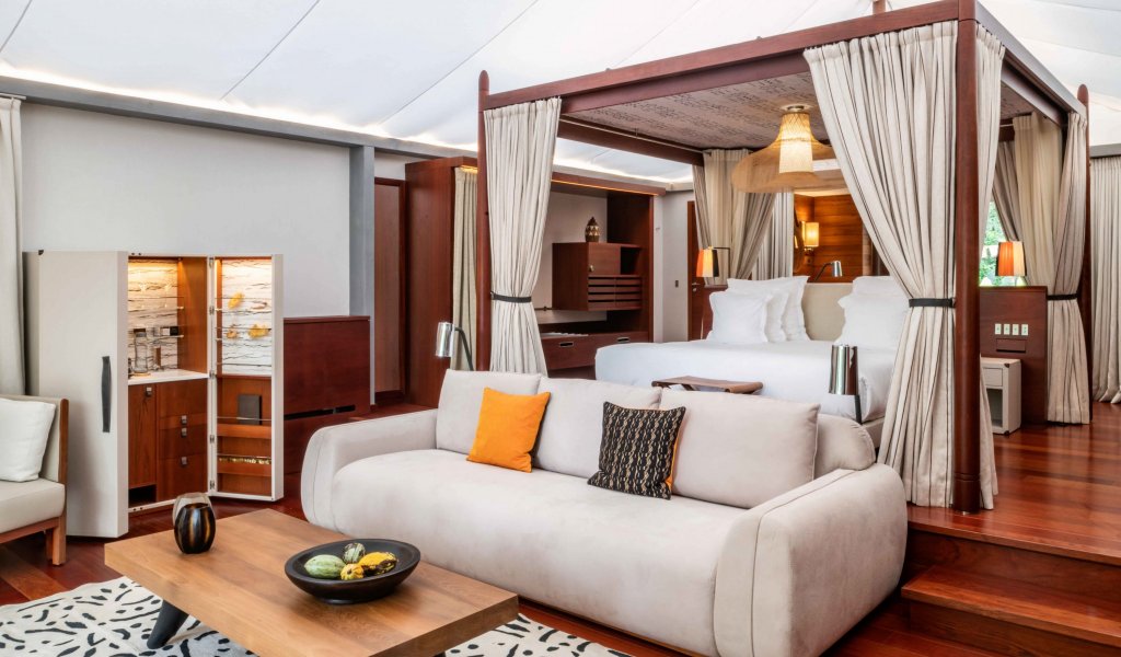 Quarto com alcatifa, mesa de apoio, sofá branco e cama de dossel ligeiramente elevada no Sundy Praia