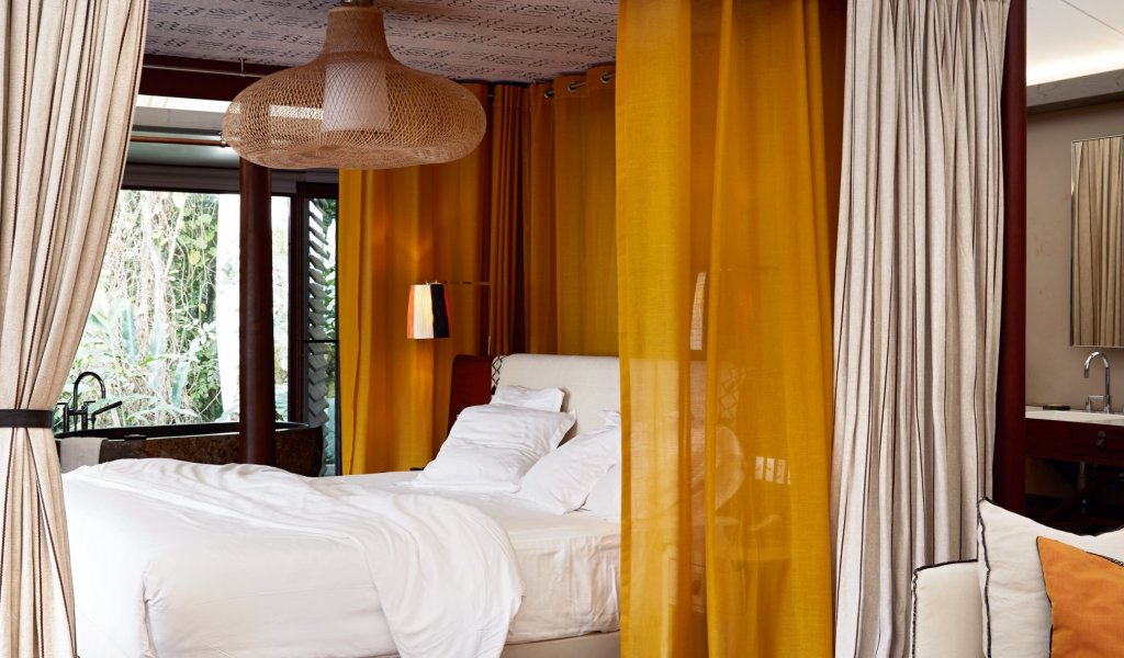 Vista da elegante cama de casal numa tenda-vila no Sundy Praia, com mesa de madeira, vasos e um tapete amarelo-preto em primeiro plano.