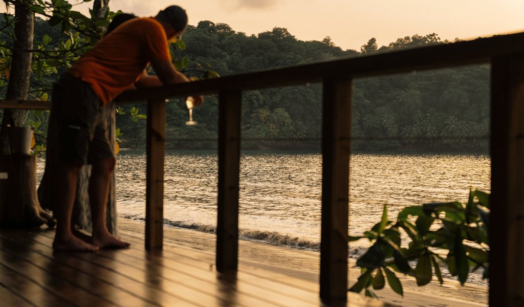 A man holding a drink at the beach during sunset at Bom Bom Beach Resort.