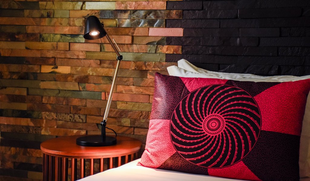 Cama com almofada vermelha estampada e parede de pedra no Omali.