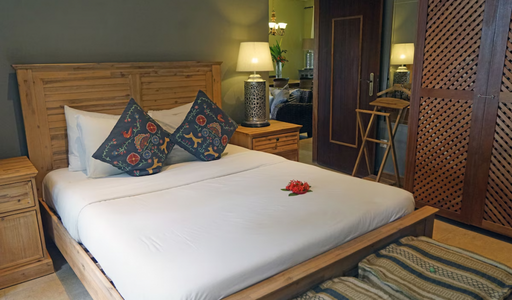 Garden Room at Belo Monte with wooden bed, crisp white linens and patterned cushions, warm lamps and wardrobe.