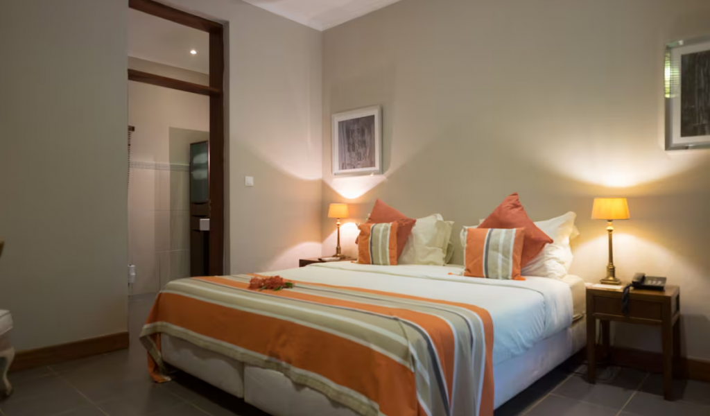 Spacious Garden Room with king bed, striped bedspread and soft lamps, doorway leading to the ensuite bathroom.